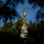 Golden statue surrounded by trees on a sunny day.