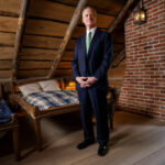 Man in suit standing in rustic attic interior.